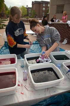 two young boys are making ice cream at an outdoor table with plastic containers on it