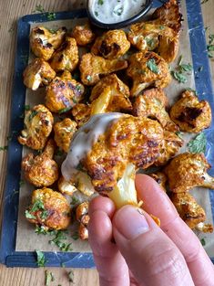 a hand holding up a piece of food on top of a blue tray with sauce