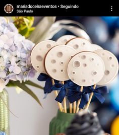 some cookies are sitting on sticks in a vase with blue ribbon and flowers behind them