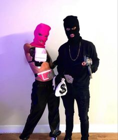 two people dressed in costumes standing next to each other on a hard wood floor with one person wearing a pink mask