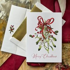 two christmas cards with red bows and holly berries on them, one has a gold envelope that says merry christmas