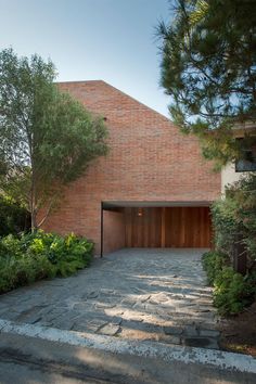 a brick house with an open garage door and driveway leading to the front entrance, surrounded by greenery