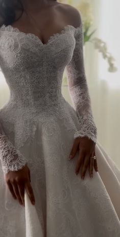 a woman in a white wedding dress with long sleeves and lace on her arms is posing for the camera