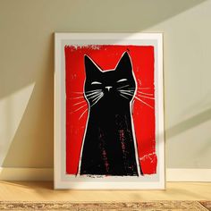 a red and black cat print on a wall next to a wooden table with a lamp