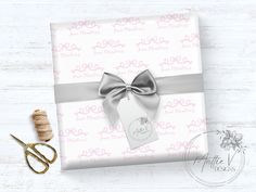 a gift wrapped in white paper with a silver ribbon and a pair of scissors next to it