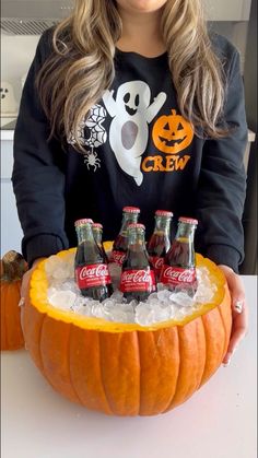 a woman is holding up a carved pumpkin with soda bottles in it and halloween decorations on top