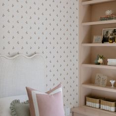 a white bed sitting next to a pink pillow on top of a wooden shelf filled with books