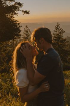 a man and woman are kissing in the mountains at sunset, with trees behind them