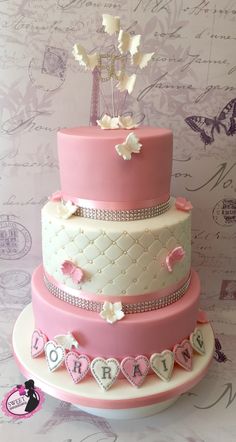 a three tiered cake with pink and white frosting on the top, decorated with hearts