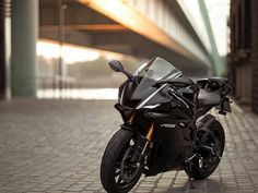 a black motorcycle parked on top of a brick road next to a building with a bridge in the background