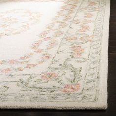 a white rug with pink and green flowers on the bottom is sitting on a wooden floor