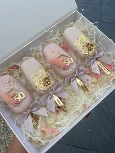 three pink and gold decorated baby booties in a white box with ribbon around them