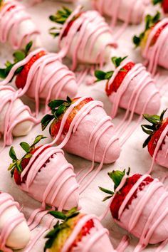 strawberries with pink icing and green leaves on them are lined up in rows