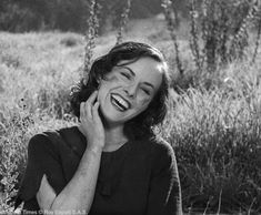 a woman sitting in the grass talking on her cell phone with a smile on her face