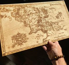 a person holding up a wooden map that looks like the middle earth is on fire