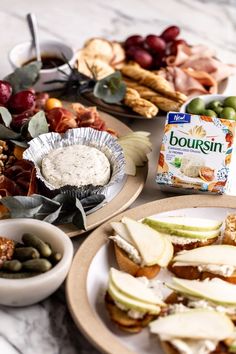 an assortment of food is displayed on plates with fruit and crackers next to them