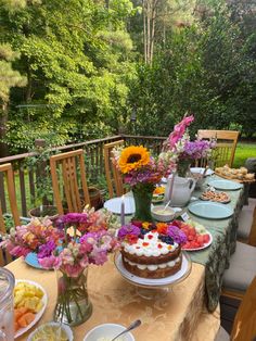 a table topped with cakes and flowers on top of a wooden table covered in plates