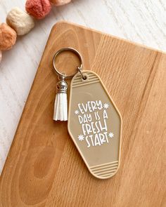 a keychain that says happy day is a fresh start on it next to some tassels