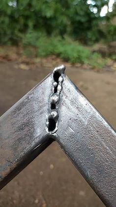 a close up of a metal rail with holes in the middle and trees in the background