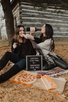 two women sitting on the ground drinking beer and eating pizza