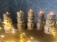 wooden snowman candles are lined up on a table with string lights around them and the top one is turned upside down