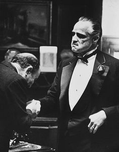 an old black and white photo of a man in a tuxedo shaking hands with another man