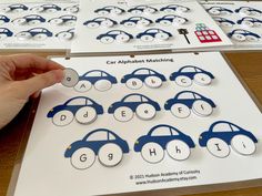 a hand is pointing at some cars on the table with matching numbers to match them