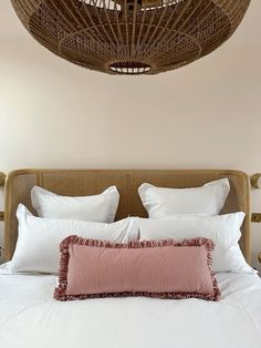 a bed with white sheets and pillows under a wicker ceiling light hanging from the ceiling