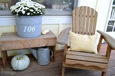 two chairs sitting on a porch next to a potted plant with white flowers in it