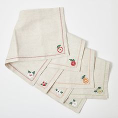 four napkins with embroidered fruit designs on them