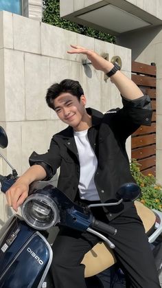 a young man sitting on top of a blue scooter with his hand in the air