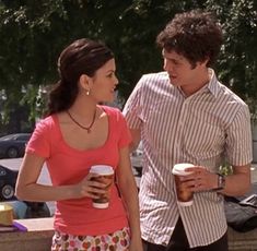 a young man and woman standing next to each other holding coffee cups in their hands