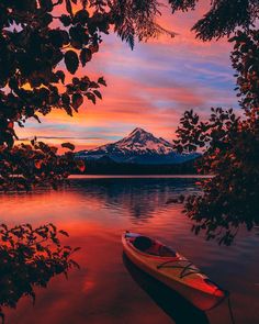 a boat sitting on top of a lake next to a tree covered shore under a colorful sky