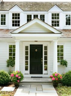 a white house with black front door and flowers on the side walk in front of it