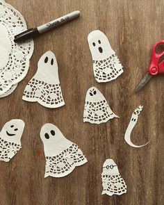 paper cut out to look like ghostes on a wooden table with scissors and markers