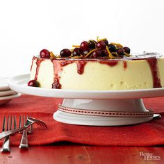 a cheesecake with cherries and orange zest is on a white cake platter