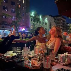 two women sitting at a table with food and drinks in front of them, taking pictures