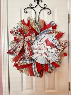 a red and white wreath with a cardinal on it is hanging on the front door