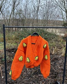 an orange sweater is hanging on a black rack in front of some leaves and trees