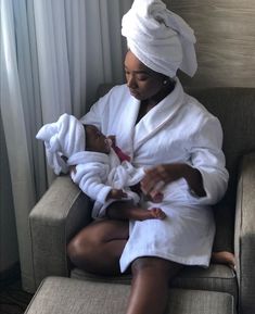 a woman sitting on a couch holding a baby in her lap and wearing a white robe