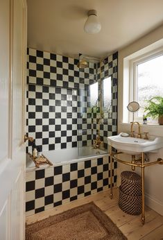 a bathroom with black and white tiles on the wall, sink and bathtub next to a window