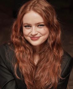 a woman with long red hair is smiling at the camera and has her arms crossed