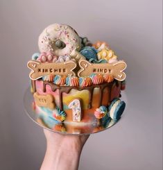 a hand holding a decorated cake with donuts and candy on it that says imagine, mindy