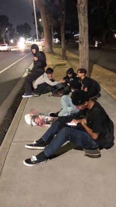 several skateboarders are sitting on the sidewalk at night