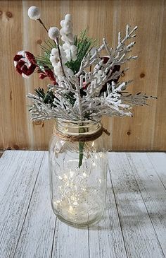 a mason jar filled with white flowers and greenery sitting on a wooden table next to a wood paneled wall