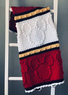 a red and white crocheted blanket hanging on a ladder next to a wall