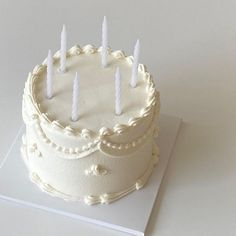 a white cake with five candles on it sitting on top of a card board in front of a white background