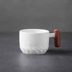 a white cup with a wooden handle sitting on a table next to a gray wall