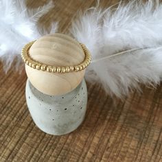 a white feather is laying next to a small jar with a gold beaded ring on it