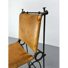 an old leather chair with wrought iron legs and back rests on a metal stand against a white wall